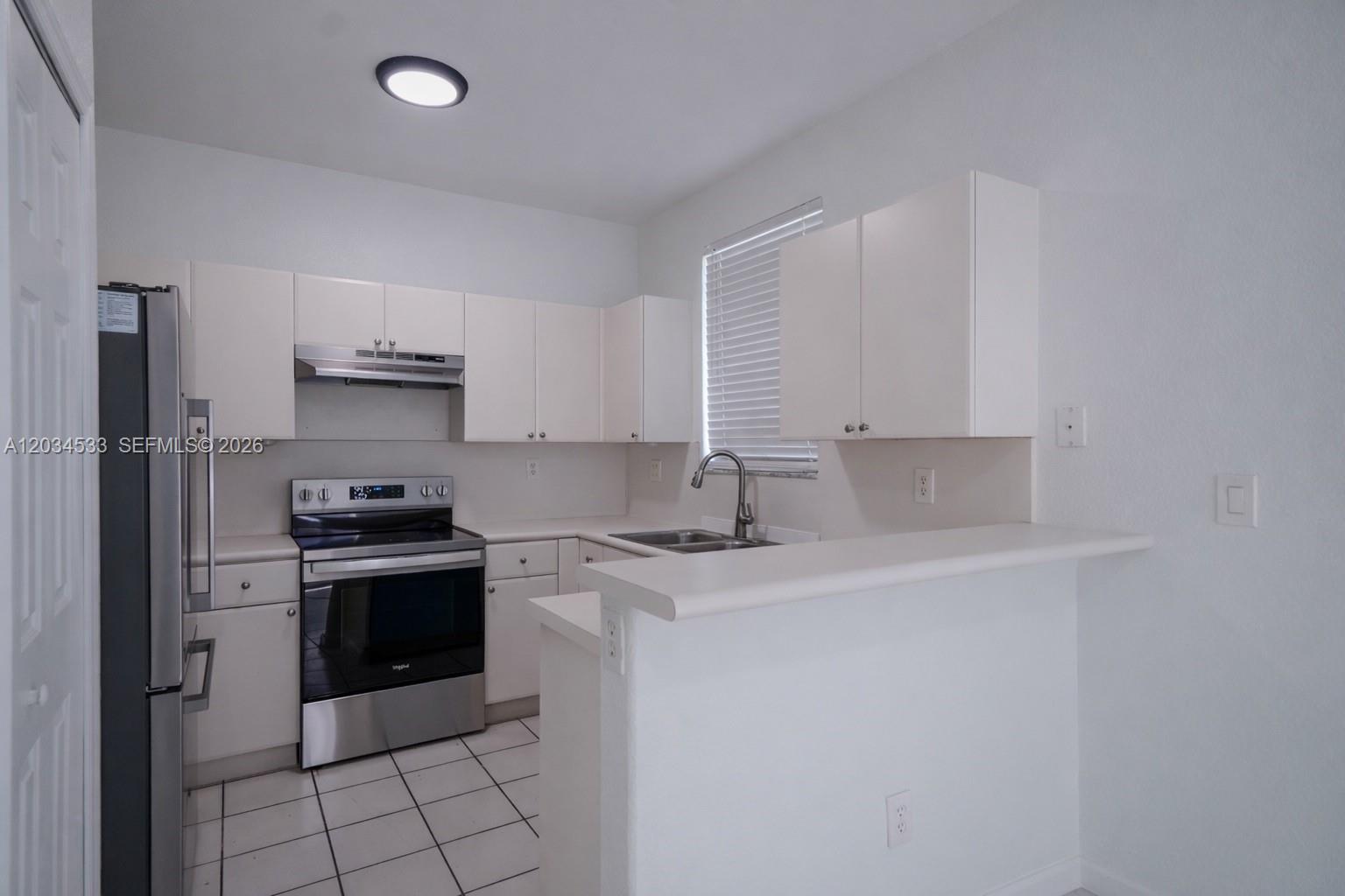 A kitchen features white cabinets, stainless steel appliances, a tile floor, and a breakfast bar — 1441 SE 24th Ct # 257, Homestead FL 33035, HOMESTEAD, FL