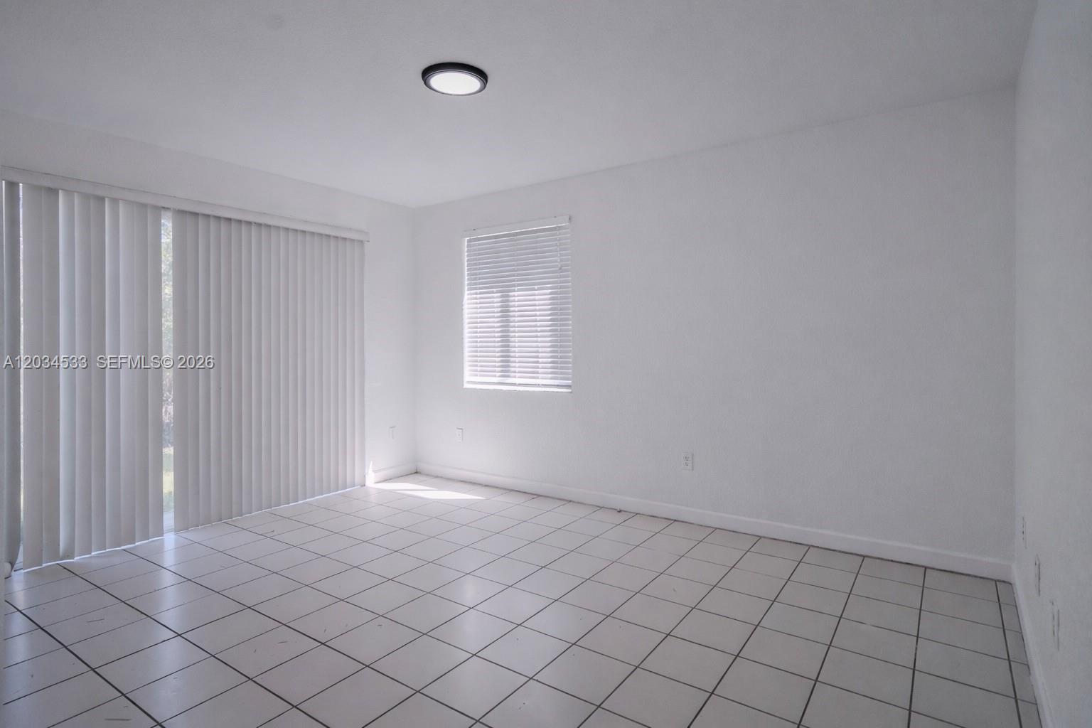 An empty room features white walls, white tile flooring, a window, and sliding glass doors — 1441 SE 24th Ct # 257, Homestead FL 33035, HOMESTEAD, FL