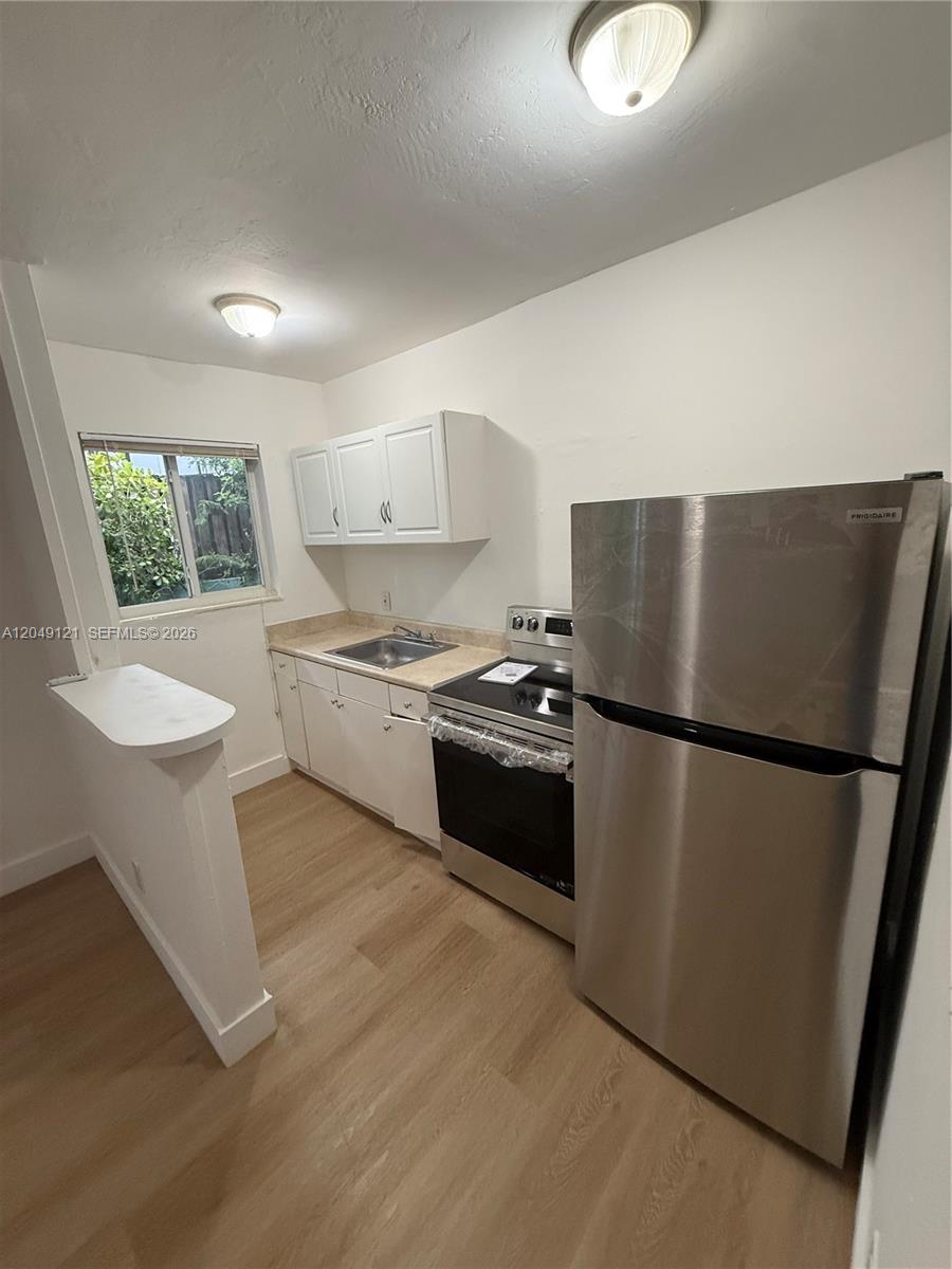 A small kitchen features white cabinets, stainless steel appliances, and light wood-look flooring — 469 SW 3rd St # 4, Miami FL 33130, MIAMI, FL