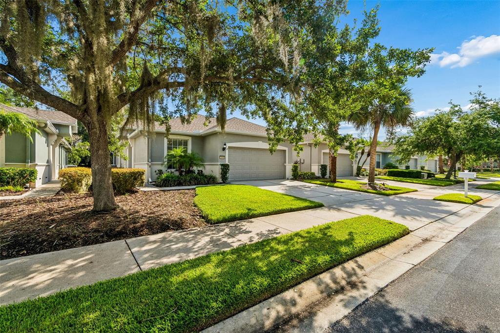 A suburban house with a two-car garage, manicured lawn, and large oak trees — 10448 48TH COURT E, PARRISH, FL