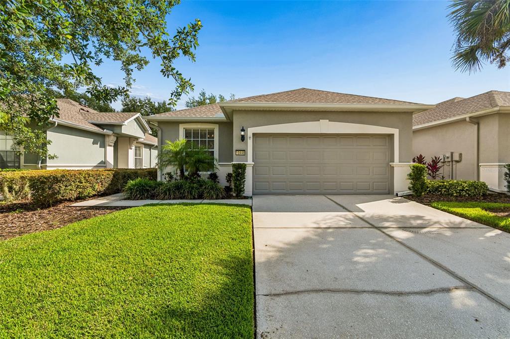 A single-story house with a two-car garage, beige stucco exterior, and a manicured front lawn — 10448 48TH COURT E, PARRISH, FL