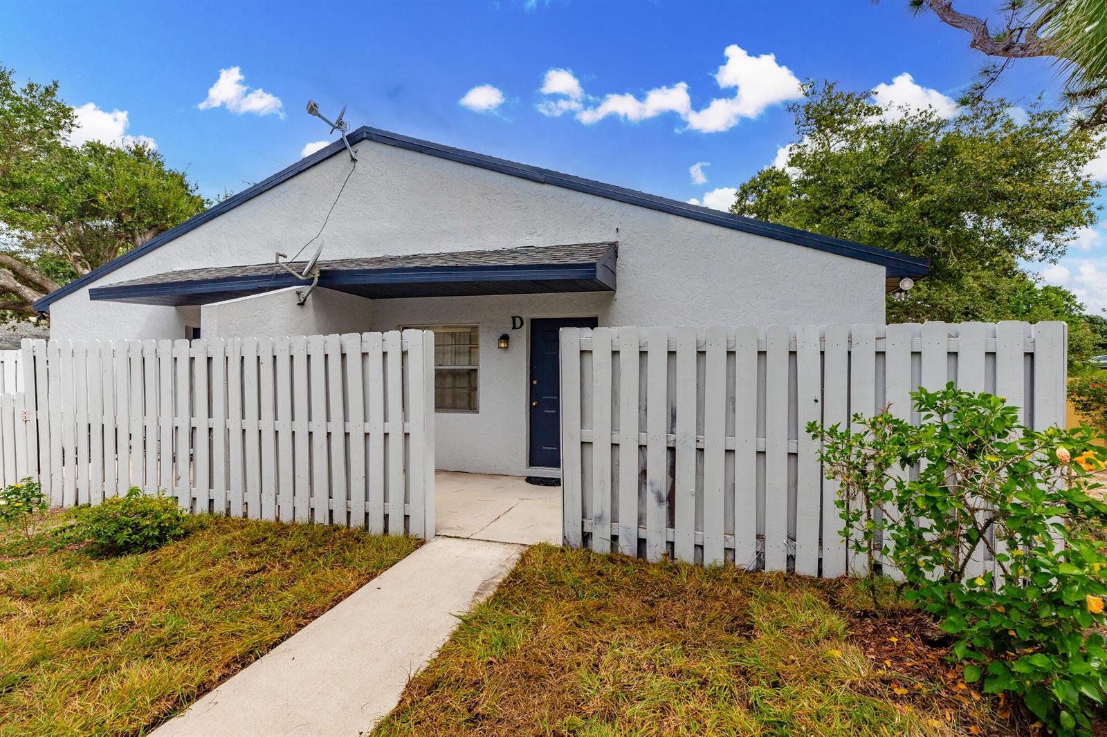 A white single-story building features a gated front courtyard and a dark blue front door — 2007 Oleander Boulevard Apt D, Fort Pierce FL 34950, FORT PIERCE, FL