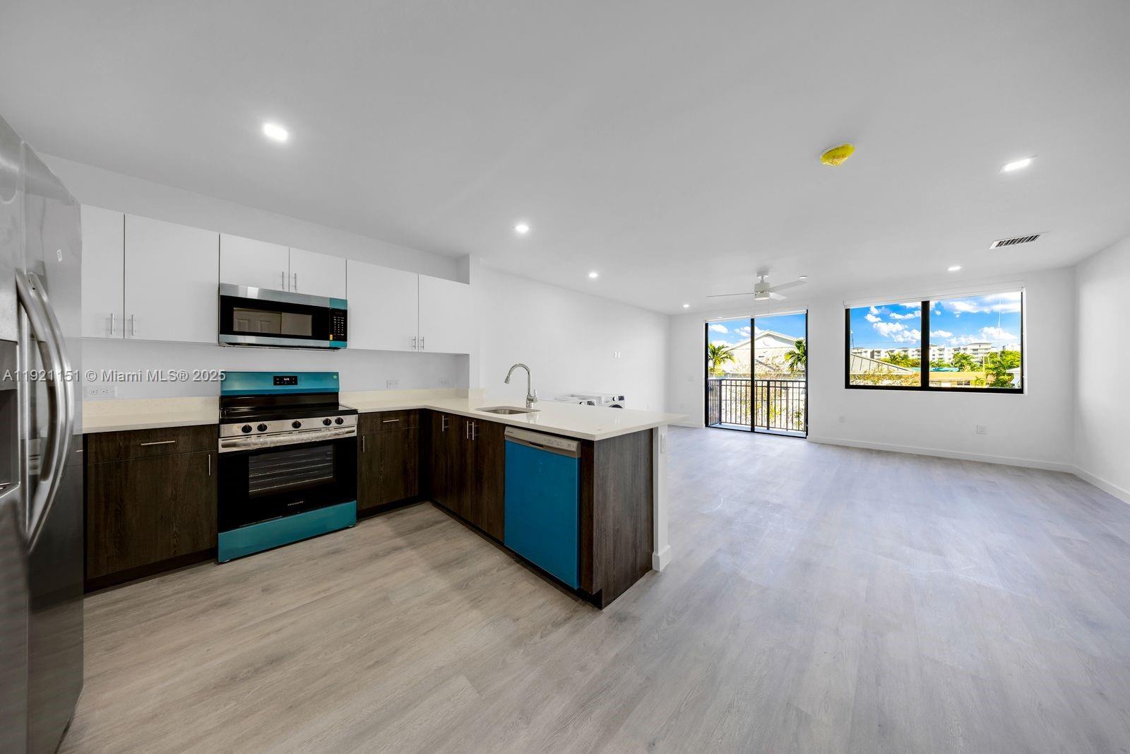 A modern kitchen with dark wood cabinets and white countertops opens into a living area — 20 NE 19th Ave # 210, Pompano Beach FL 33060, POMPANO BEACH, FL