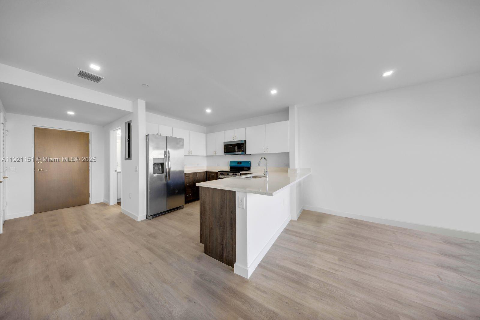 A modern kitchen features white cabinetry, stainless steel appliances, and a wood-paneled island countertop — 20 NE 19th Ave # 210, Pompano Beach FL 33060, POMPANO BEACH, FL