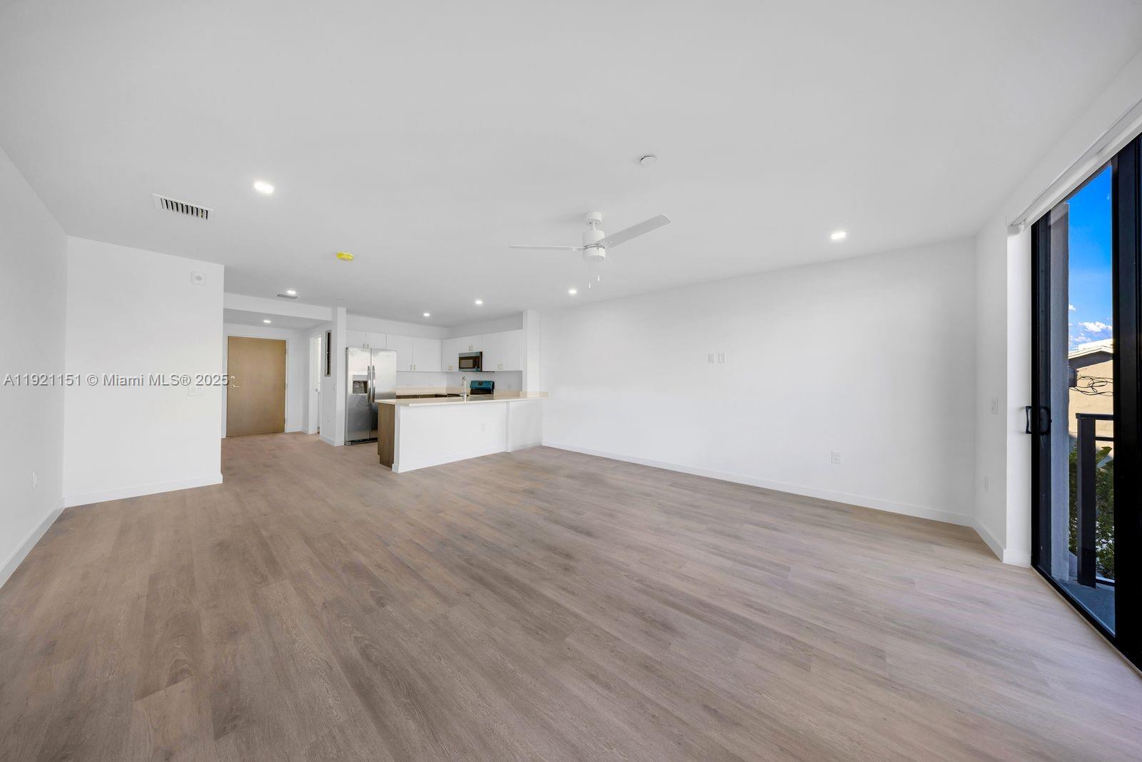 An open-concept living area features light wood-look flooring, white walls, and a modern kitchen — 20 NE 19th Ave # 210, Pompano Beach FL 33060, POMPANO BEACH, FL