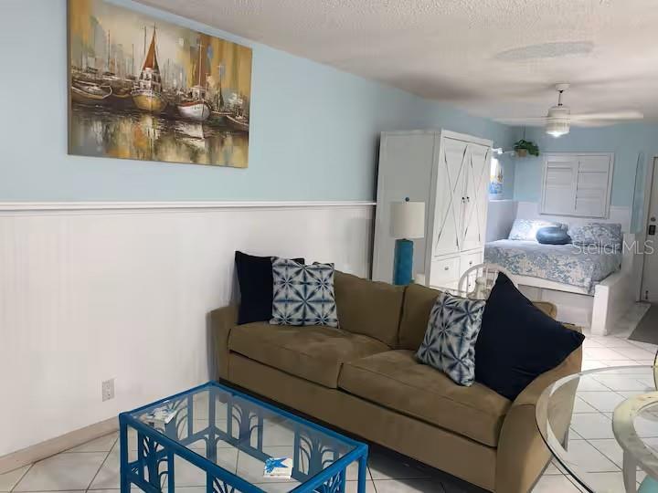 A living room with a brown sofa, blue coffee table, and a bed in the background — 800 BAYWAY BOULEVARD UNIT 26, CLEARWATER BEACH, FL