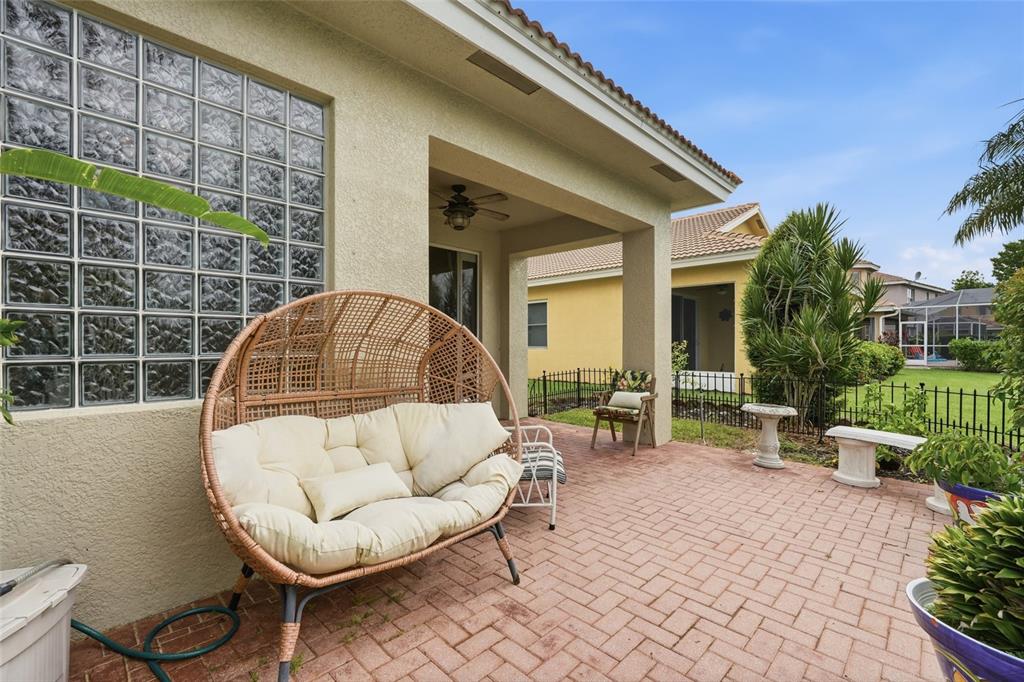 A covered brick patio features a wicker egg chair, glass block windows, and backyard views — 3565 MALAGROTTA CIRCLE, CAPE CORAL, FL