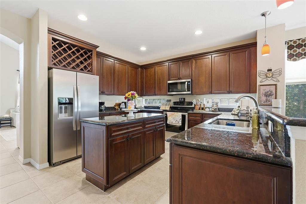 A kitchen features dark wood cabinets, granite countertops, a center island, and stainless steel appliances — 3565 MALAGROTTA CIRCLE, CAPE CORAL, FL