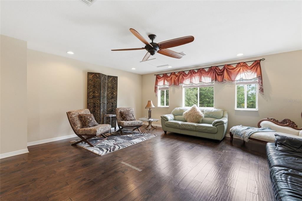 A living room features dark wood flooring, a ceiling fan, and various seating arrangements — 3565 MALAGROTTA CIRCLE, CAPE CORAL, FL