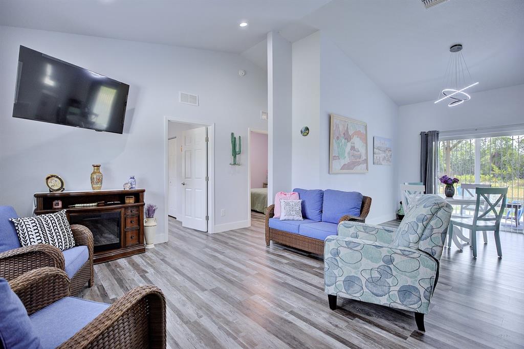 A living room features wood-look flooring, a fireplace console, wicker furniture, and a dining area — 230 E CANAL WAY NE, LAKE PLACID, FL