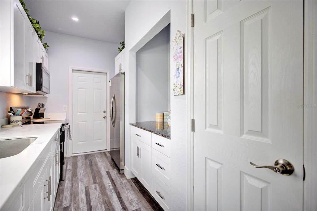 A kitchen features white cabinets, stainless steel appliances, granite countertops, and wood-look flooring — 230 E CANAL WAY NE, LAKE PLACID, FL
