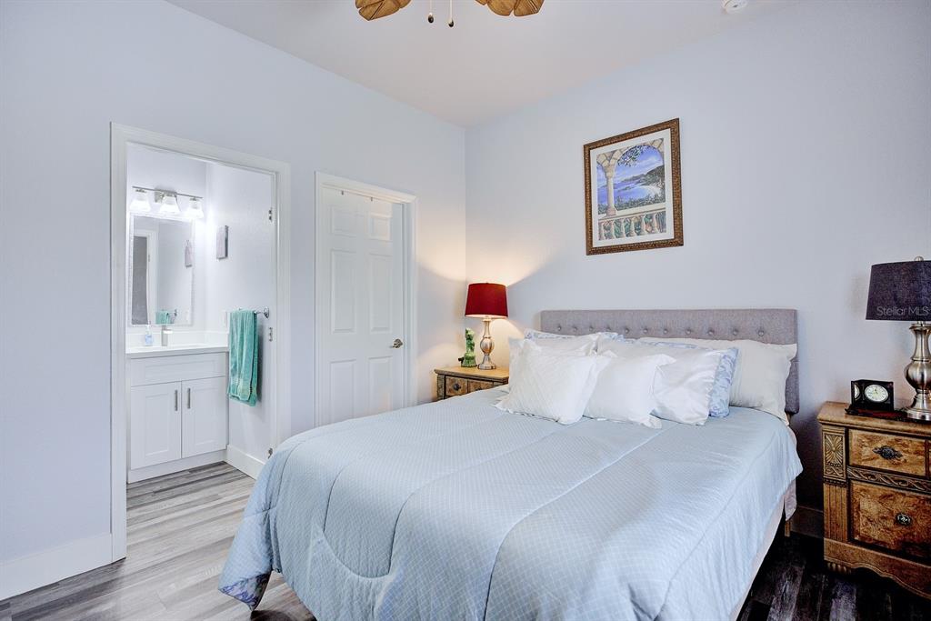 A bedroom features a bed with a light blue comforter, an attached bathroom, and wood-look flooring — 230 E CANAL WAY NE, LAKE PLACID, FL