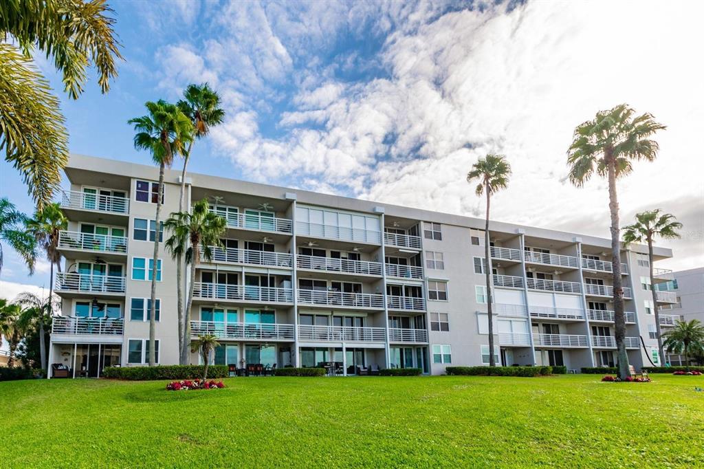 A multi-story apartment building features balconies and palm trees set against a grassy lawn — 5701 BAHIA DEL MAR CIRCLE UNIT 403, ST PETERSBURG, FL
