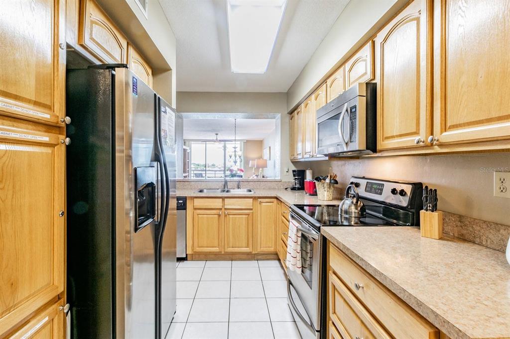 A galley-style kitchen features light wood cabinets, stainless steel appliances, and a pass-through window — 5701 BAHIA DEL MAR CIRCLE UNIT 403, ST PETERSBURG, FL