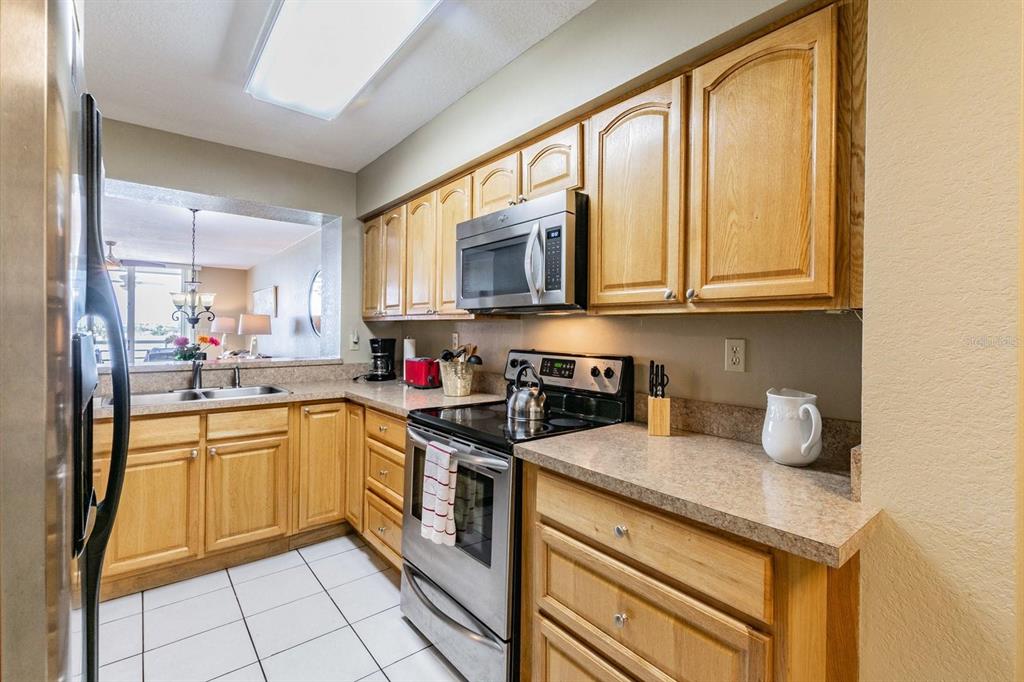 A kitchen features light wood cabinets, stainless steel appliances, and a pass-through window — 5701 BAHIA DEL MAR CIRCLE UNIT 403, ST PETERSBURG, FL
