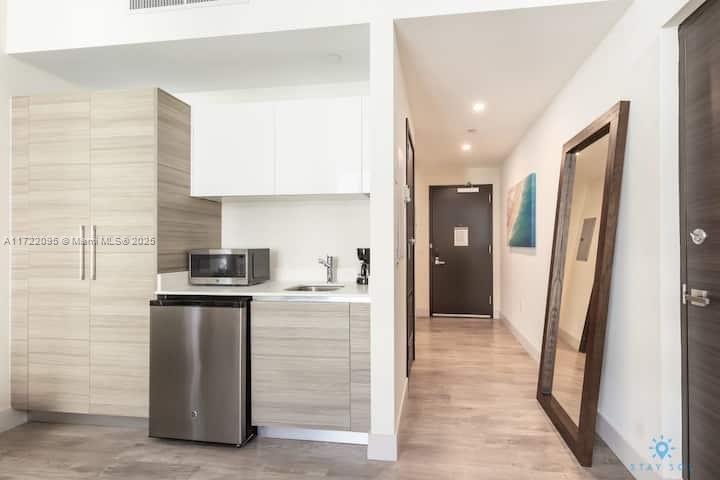 A kitchenette with light wood cabinets, a mini-fridge, and a microwave next to a hallway — 777 N Ocean Dr # S228, Hollywood FL 33019, HOLLYWOOD, FL