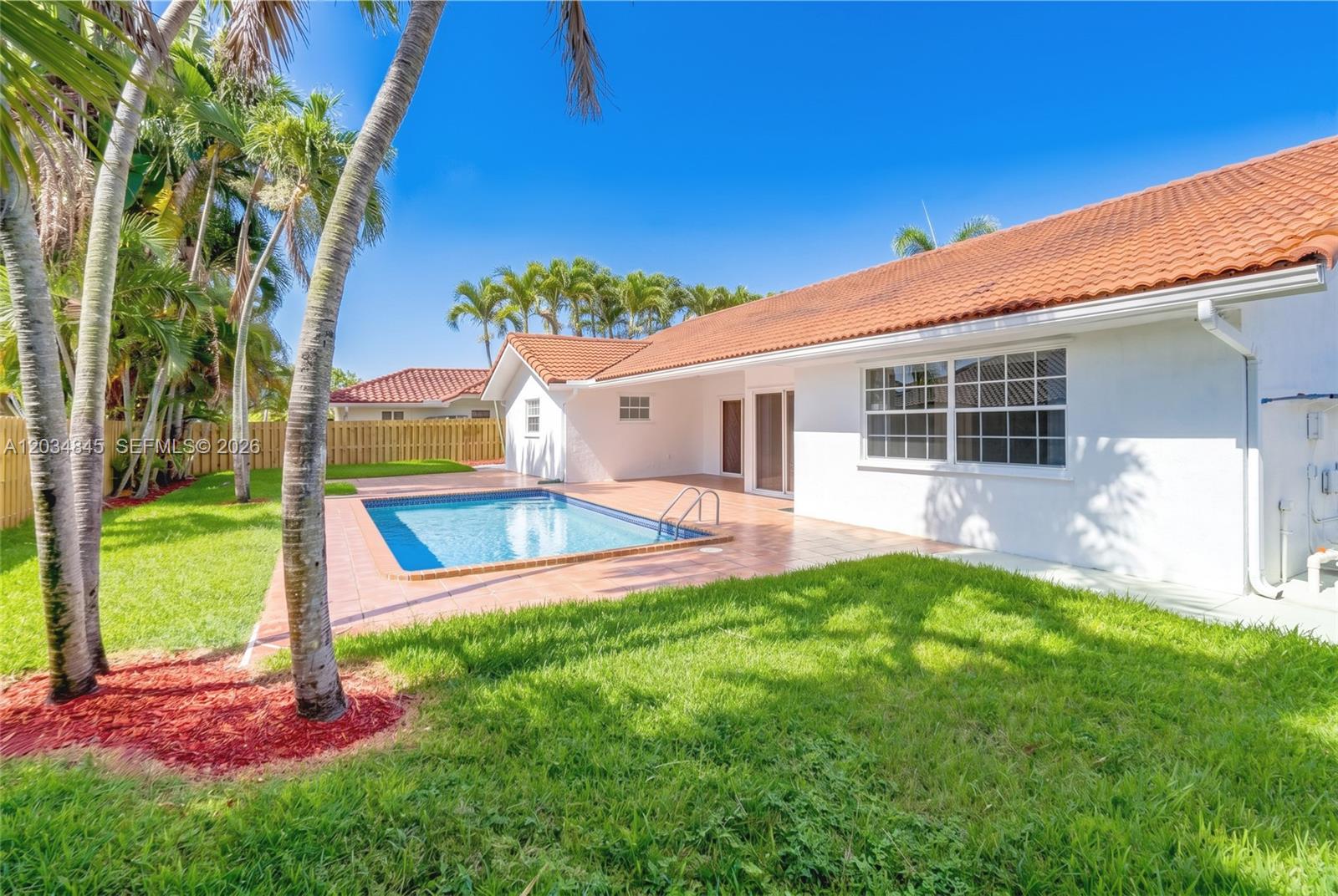 A backyard features a swimming pool, a tiled patio, and a white house with a roof — 14161 SW 153rd Ave, Miami FL 33196, MIAMI, FL
