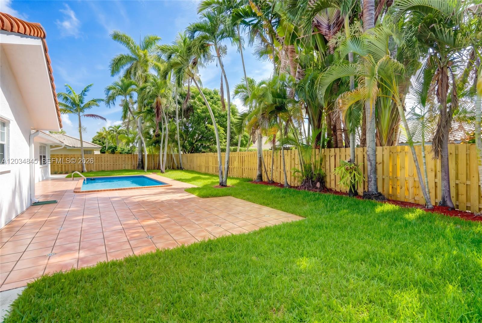 A backyard features a swimming pool, a tiled patio, and palm trees along a wooden fence — 14161 SW 153rd Ave, Miami FL 33196, MIAMI, FL