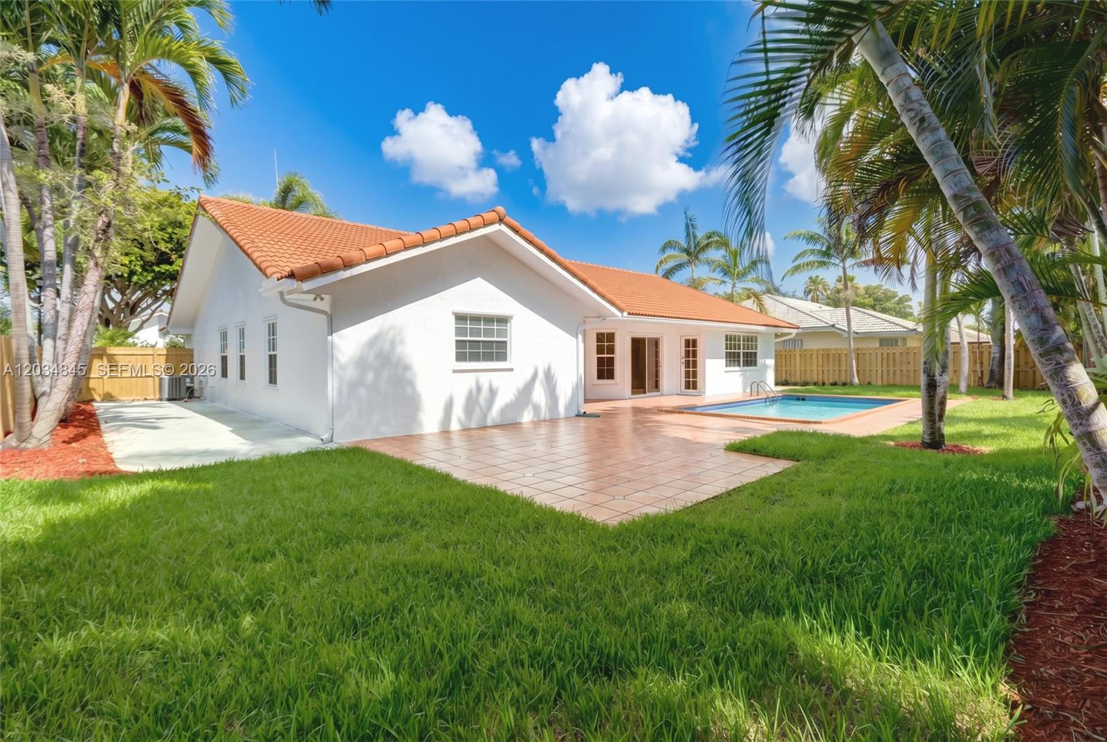 A white house with a red tile roof features a backyard pool and patio area — 14161 SW 153rd Ave, Miami FL 33196, MIAMI, FL
