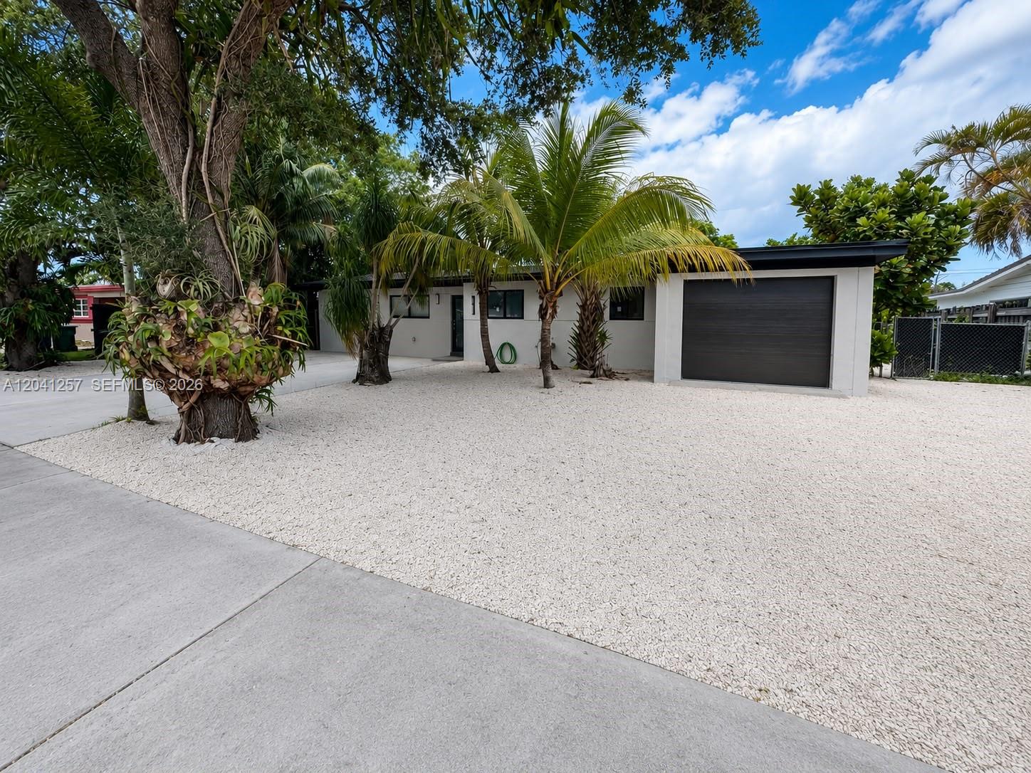 A single-story house with a gravel front yard, palm trees, and a dark garage door — 19700 NE 11th Pl, Miami FL 33179, MIAMI, FL