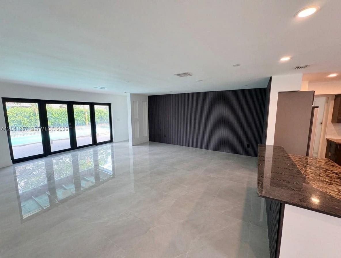 A spacious room features large glass doors, light tile flooring, and a dark slatted accent wall — 19700 NE 11th Pl, Miami FL 33179, MIAMI, FL