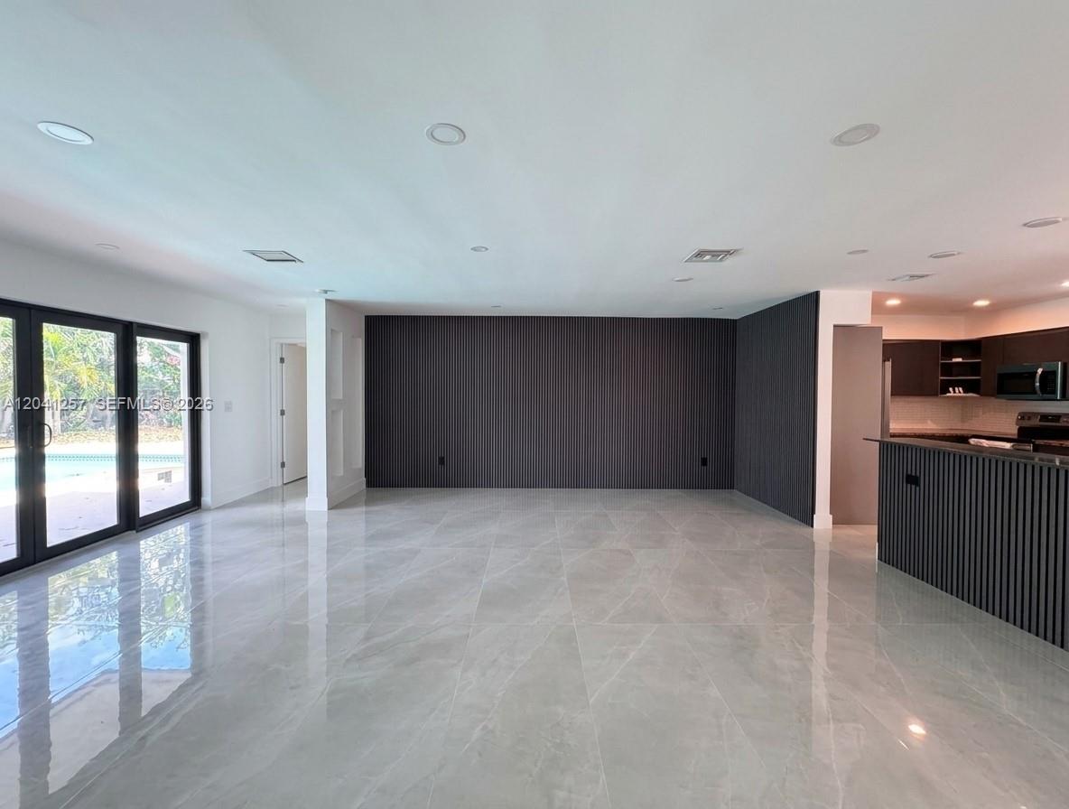 A modern open-plan living area features large glass doors, light tile flooring, and a dark slatted accent wall — 19700 NE 11th Pl, Miami FL 33179, MIAMI, FL