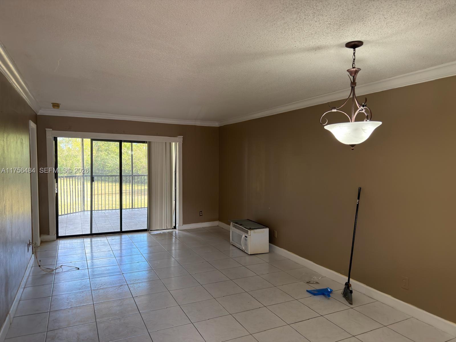 A room with tan walls, white tile flooring, a hanging light fixture, and a sliding door — 3400 Foxcroft Rd # 212, Miramar FL 33025, MIRAMAR, FL