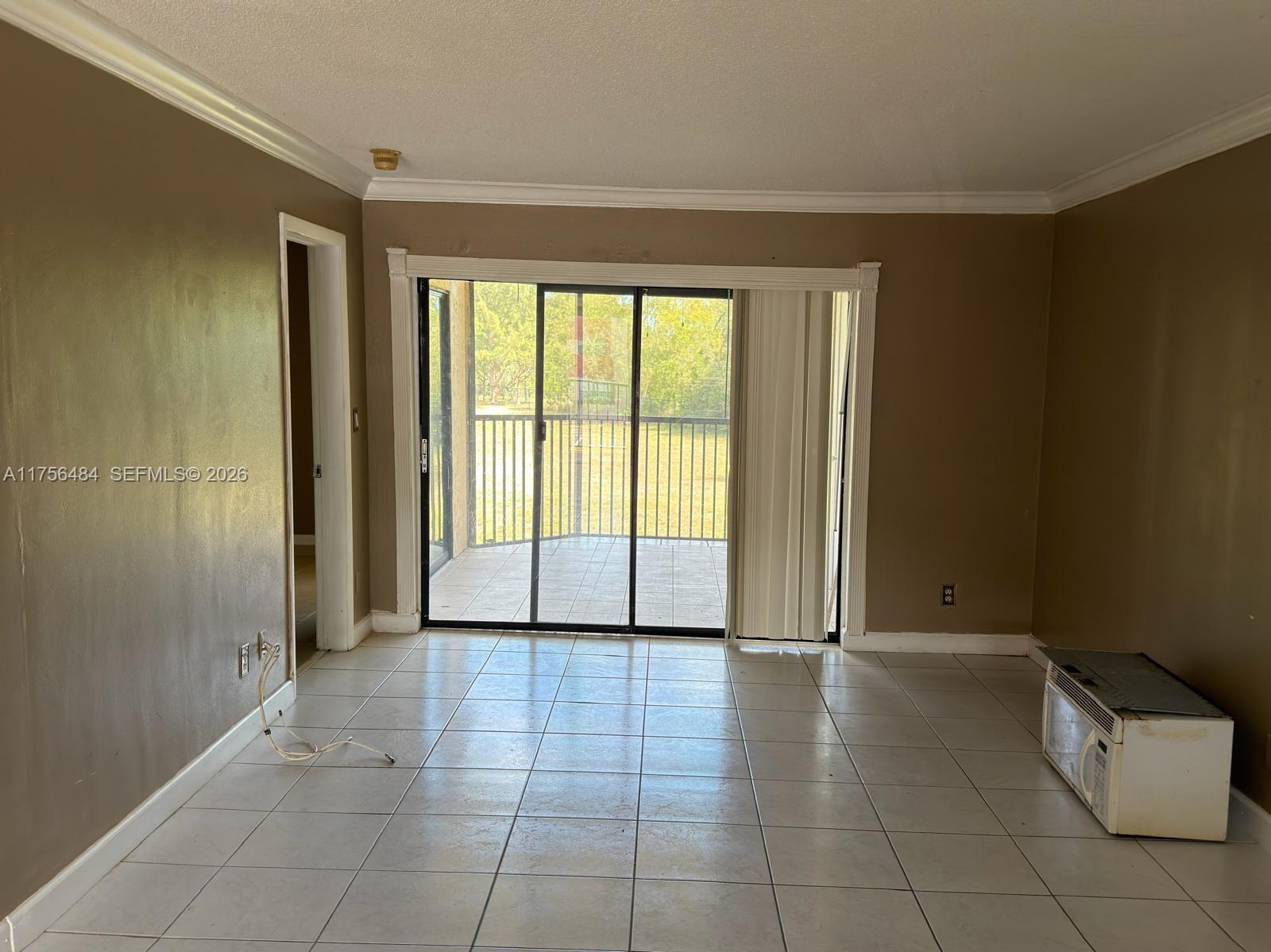 An empty room with tiled floors, brown walls, and sliding glass doors leading to a balcony — 3400 Foxcroft Rd # 212, Miramar FL 33025, MIRAMAR, FL