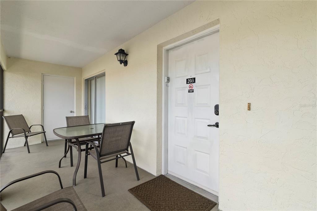 A covered balcony features a dining set, a white door labeled 203, and a wall-mounted light — 1531 PLACIDA ROAD UNIT 203, ENGLEWOOD, FL