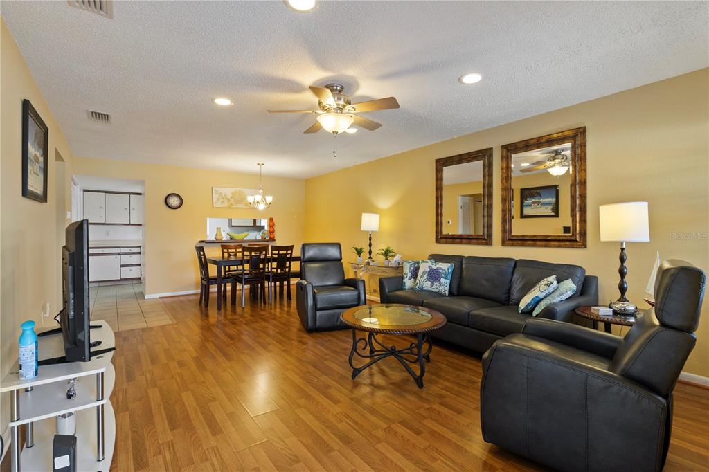A living room with hardwood floors, a black leather sofa, and an adjacent dining area — 1531 PLACIDA ROAD UNIT 203, ENGLEWOOD, FL