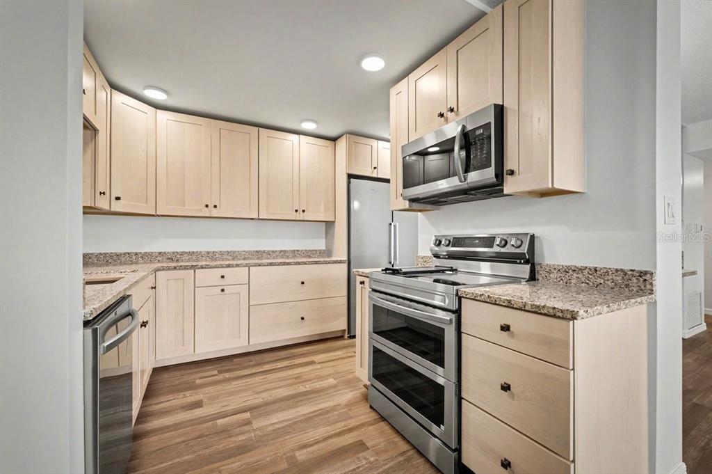 A kitchen features light wood cabinets, granite countertops, stainless steel appliances, and wood-look flooring — 1224 S PENINSULA DRIVE UNIT 621, DAYTONA BEACH, FL