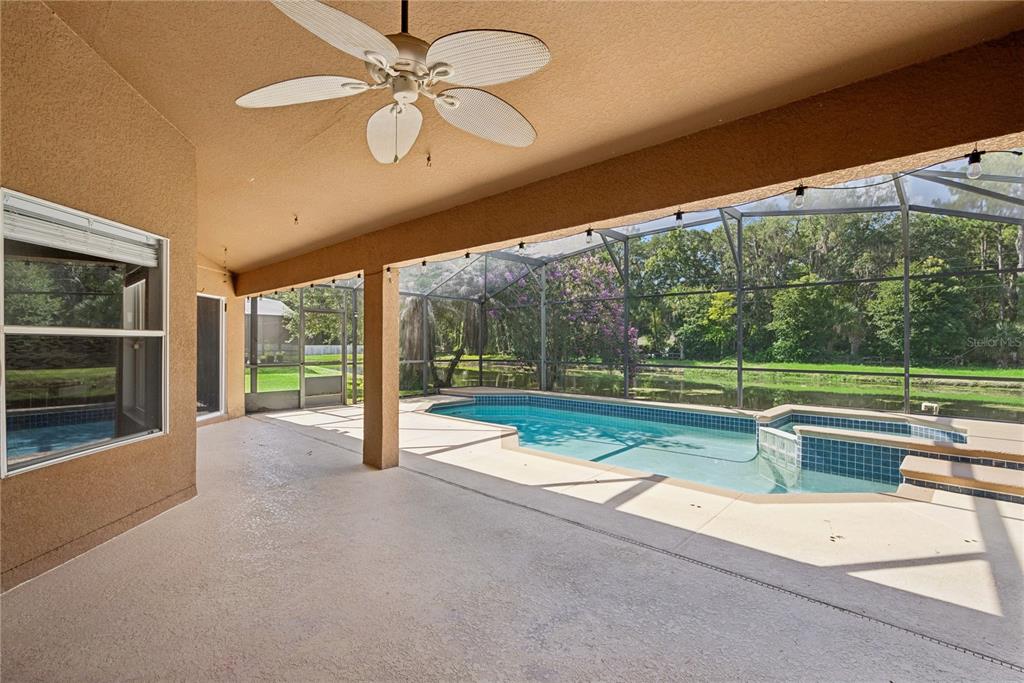A covered patio overlooks a screened-in swimming pool and spa with a view of trees — 5703 AUTUMN CHASE CIRCLE, SANFORD, FL