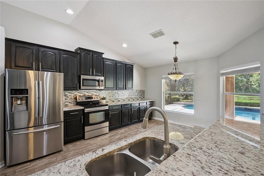 A kitchen features dark wood cabinets, stainless steel appliances, granite countertops, and a pool view — 5703 AUTUMN CHASE CIRCLE, SANFORD, FL