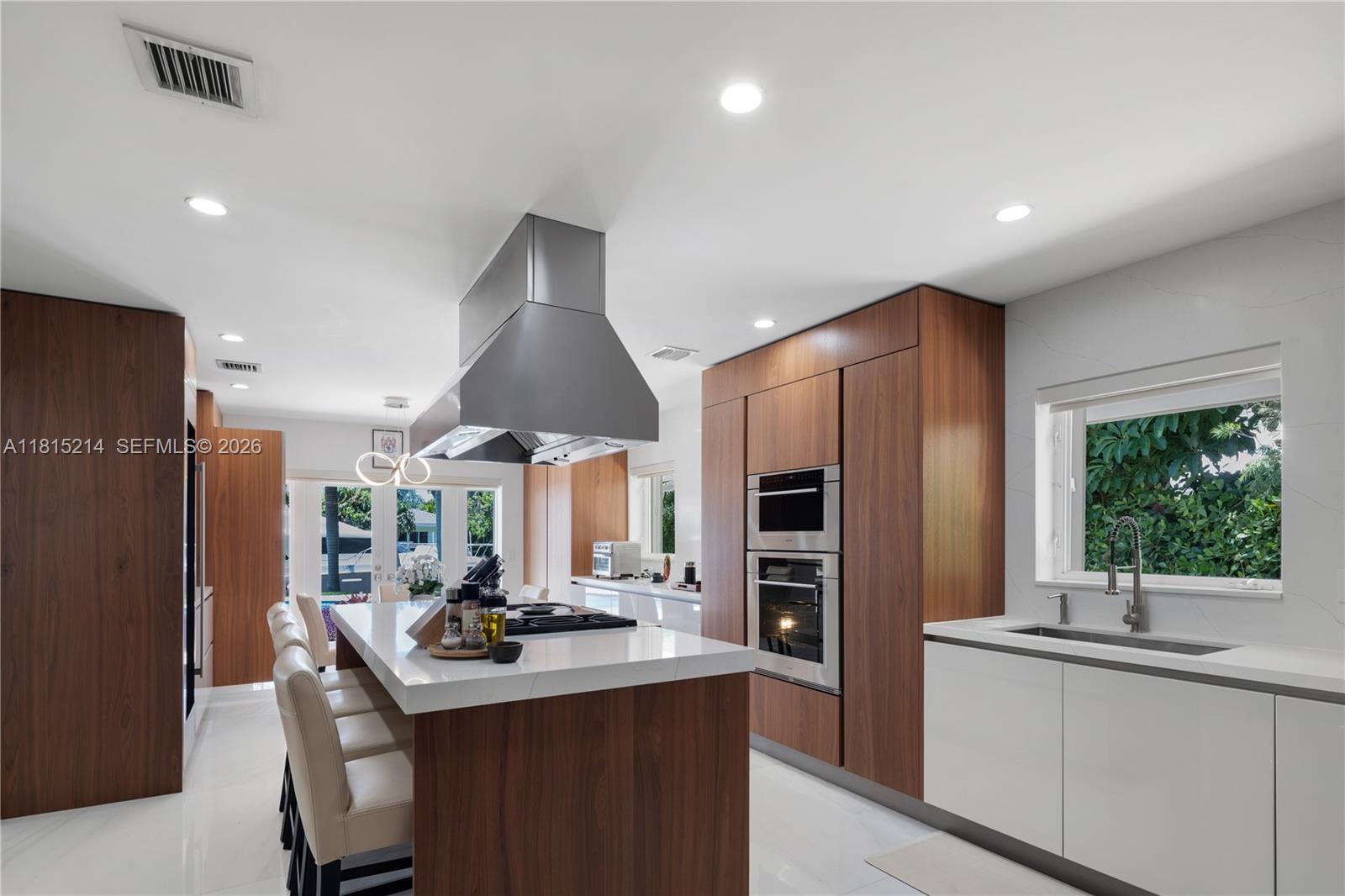 A modern kitchen features a large wood-paneled island, stainless steel appliances, and white cabinetry — 435 Marquesa Dr, Coral Gables FL 33156, CORAL GABLES, FL