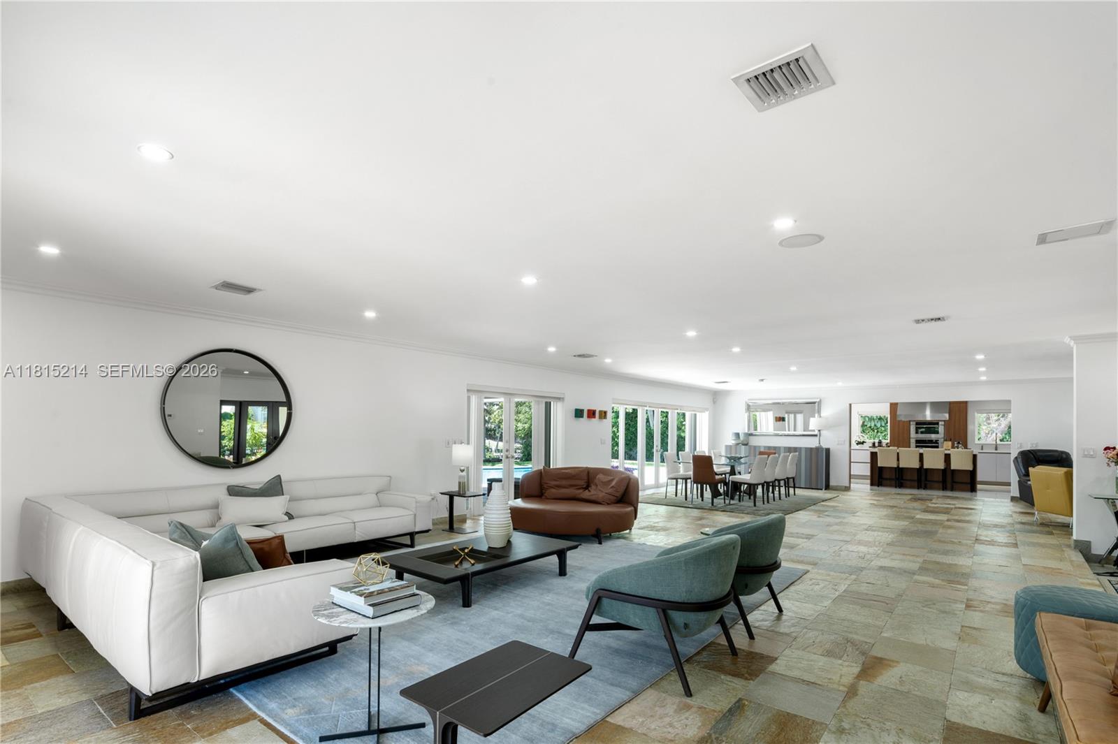 A spacious open-concept living and dining area features stone tile flooring and white walls — 435 Marquesa Dr, Coral Gables FL 33156, CORAL GABLES, FL