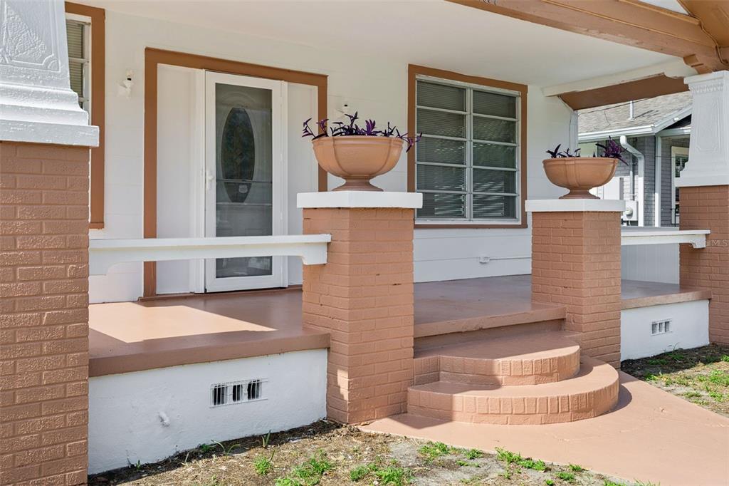 A front porch with brick columns, a white door, and two planters on a house — 1017 E 23RD AVENUE, TAMPA, FL