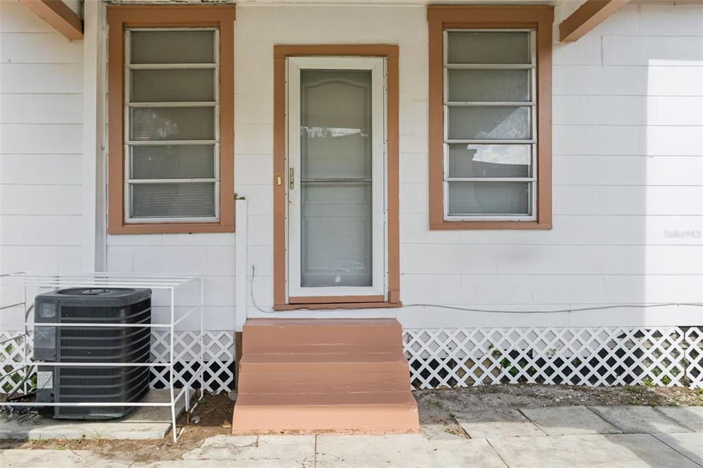 A white house exterior features a central storm door, two windows, and concrete steps — 1017 E 23RD AVENUE, TAMPA, FL