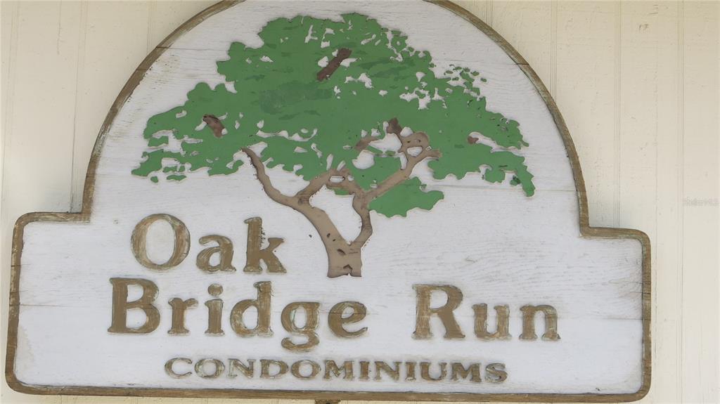 A wooden sign for Oak Bridge Run Condominiums features a painted green tree illustration — 12425 TOUCHTON DR UNIT 87, TAMPA, FL