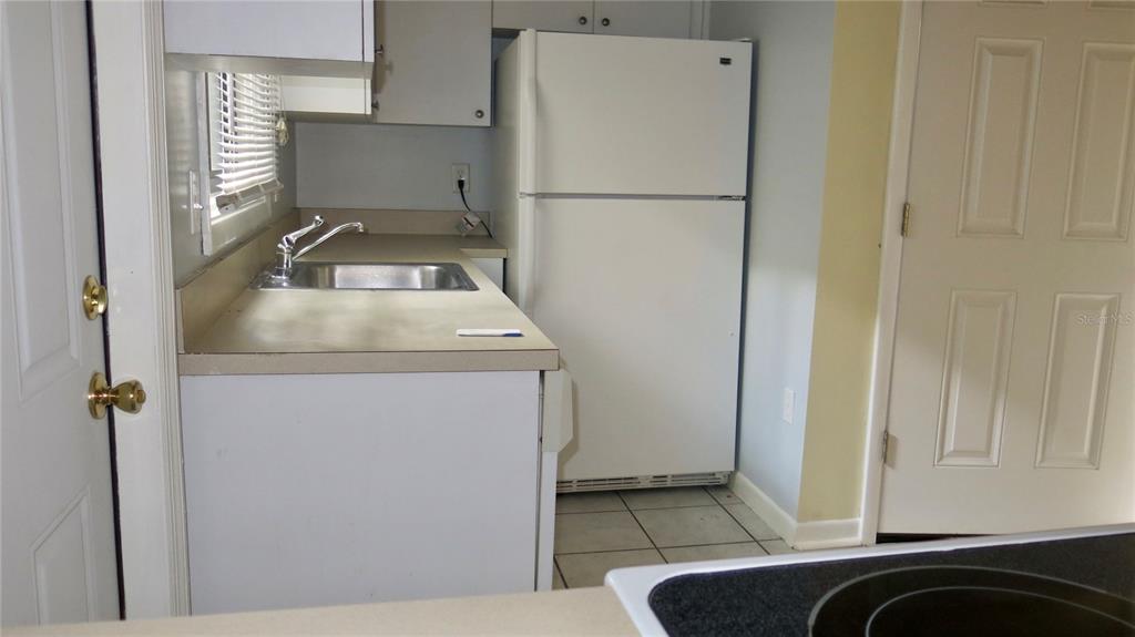A kitchen features white cabinets, a stainless steel sink, a white refrigerator, and tiled flooring — 12425 TOUCHTON DR UNIT 87, TAMPA, FL