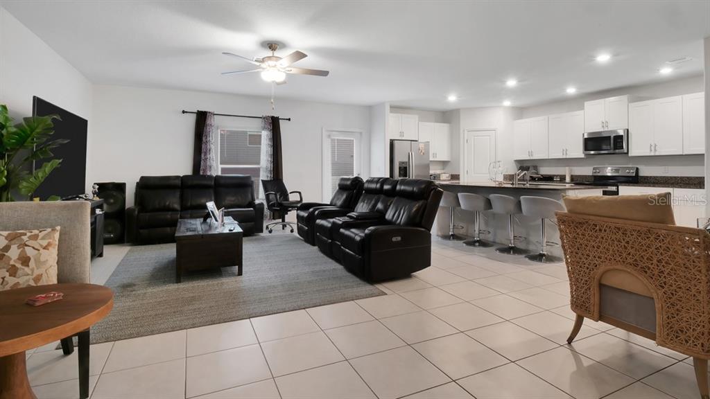 An open-concept living room and kitchen with tile flooring, black leather seating, and white cabinetry — 6300 BEVERLY HILLS DRIVE, ZEPHYRHILLS, FL