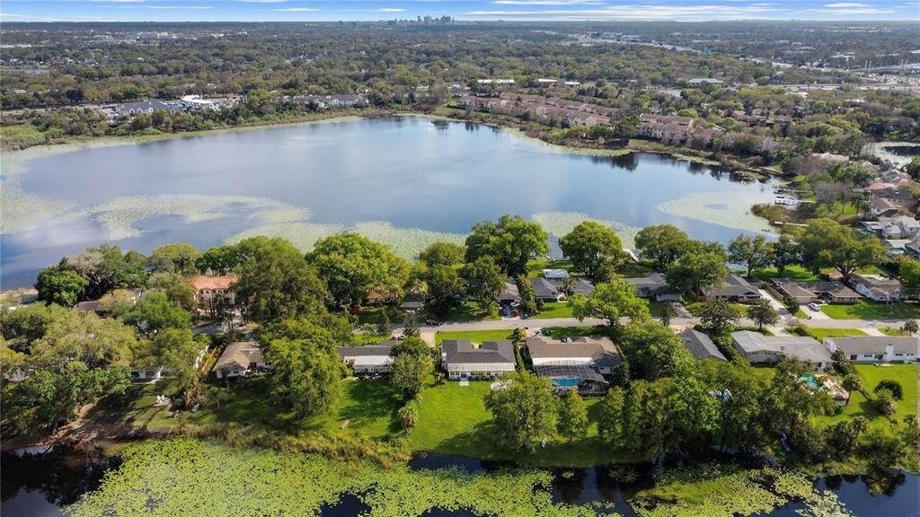 An aerial view shows houses along a lakefront with trees and a distant city skyline — 1501 DRUID ISLE ROAD, MAITLAND, FL
