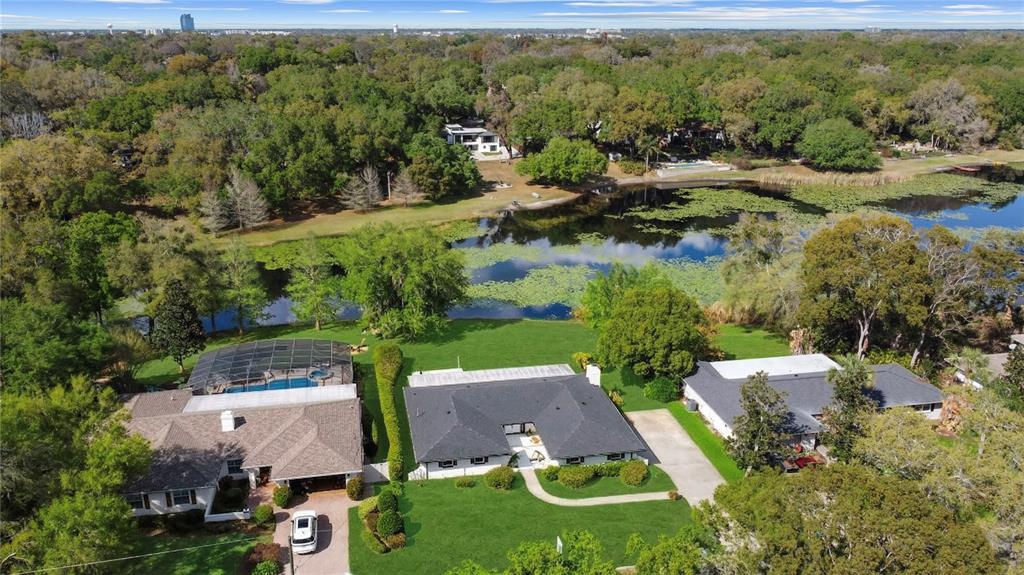 An aerial view shows three houses with lawns and pools situated along a lily-covered lake — 1501 DRUID ISLE ROAD, MAITLAND, FL