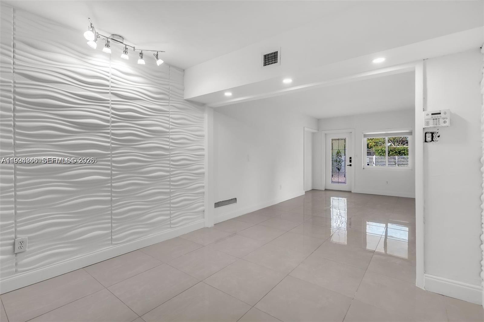A bright room features white tile floors, a textured accent wall, and recessed lighting — 3800 Charles Ter, Miami FL 33133, MIAMI, FL