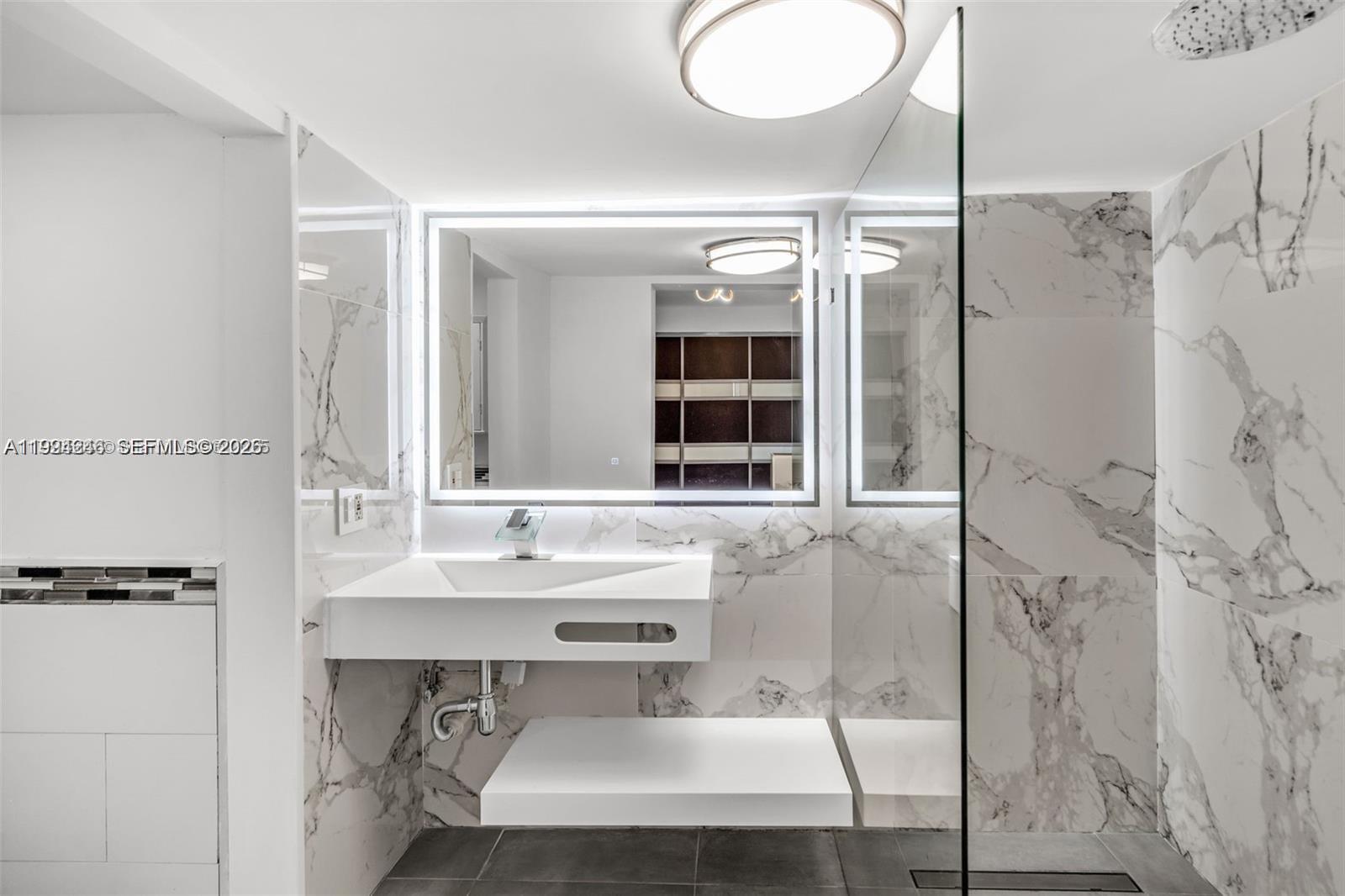 A modern bathroom features a floating vanity, a backlit mirror, and marble-patterned wall tiles — 3800 Charles Ter, Miami FL 33133, MIAMI, FL