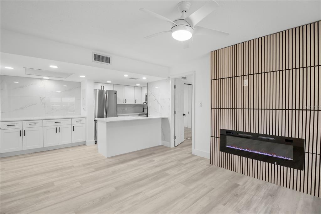 A modern kitchen and living area featuring white cabinetry, marble-style backsplashes, and a slatted wood fireplace — 4754 MARINE PARKWAY UNIT 103, NEW PORT RICHEY, FL