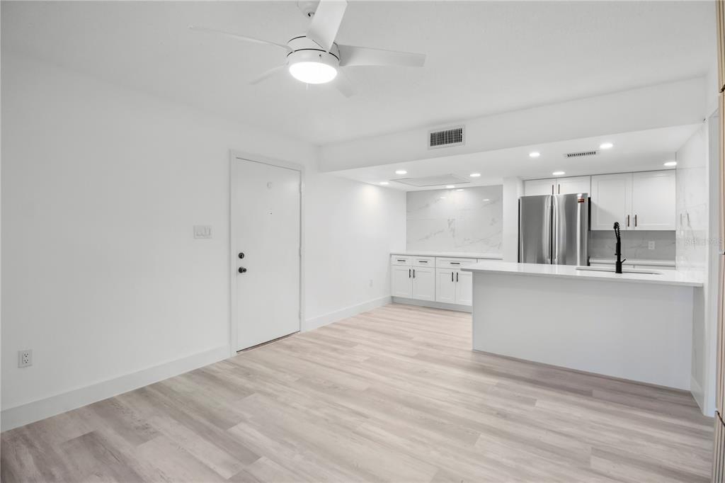 A bright kitchen and living area features white cabinetry, stainless steel appliances, and light flooring — 4754 MARINE PARKWAY UNIT 103, NEW PORT RICHEY, FL