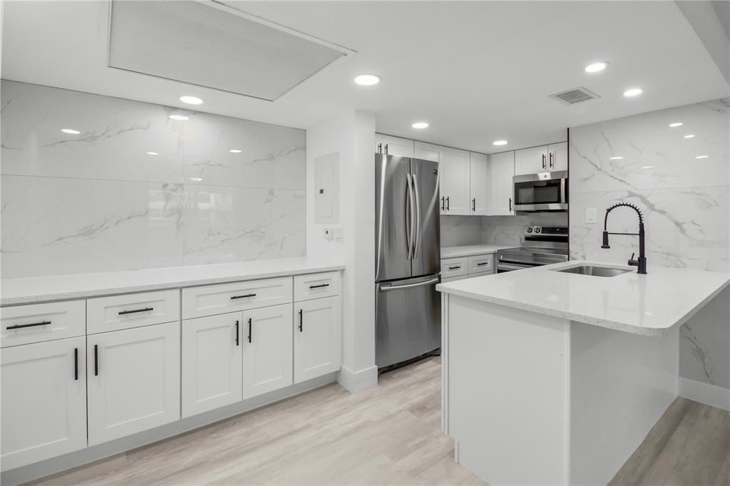 A modern kitchen features white cabinets, quartz countertops, marble-look backsplash, and stainless steel appliances — 4754 MARINE PARKWAY UNIT 103, NEW PORT RICHEY, FL
