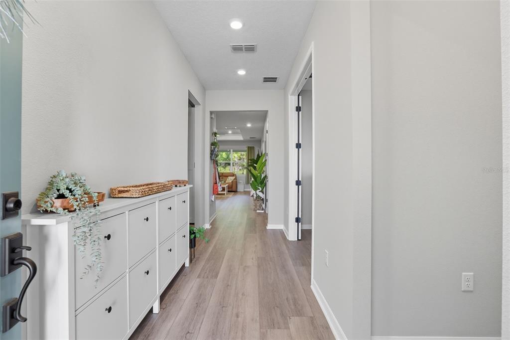 A hallway with light wood-look flooring, a white shoe cabinet, and a view into a living area — 2761 TOP HILL COURT, MINNEOLA, FL
