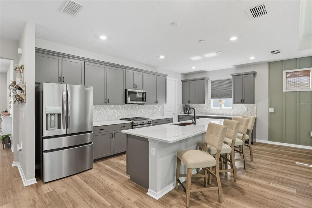 A modern kitchen features gray cabinets, white marble countertops, a center island, and stainless appliances — 2761 TOP HILL COURT, MINNEOLA, FL