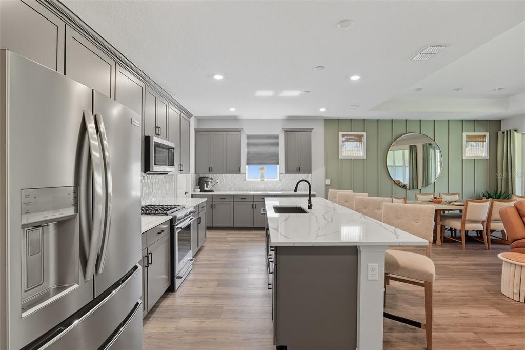A modern kitchen features gray cabinetry, a white quartz island, and stainless steel appliances — 2761 TOP HILL COURT, MINNEOLA, FL